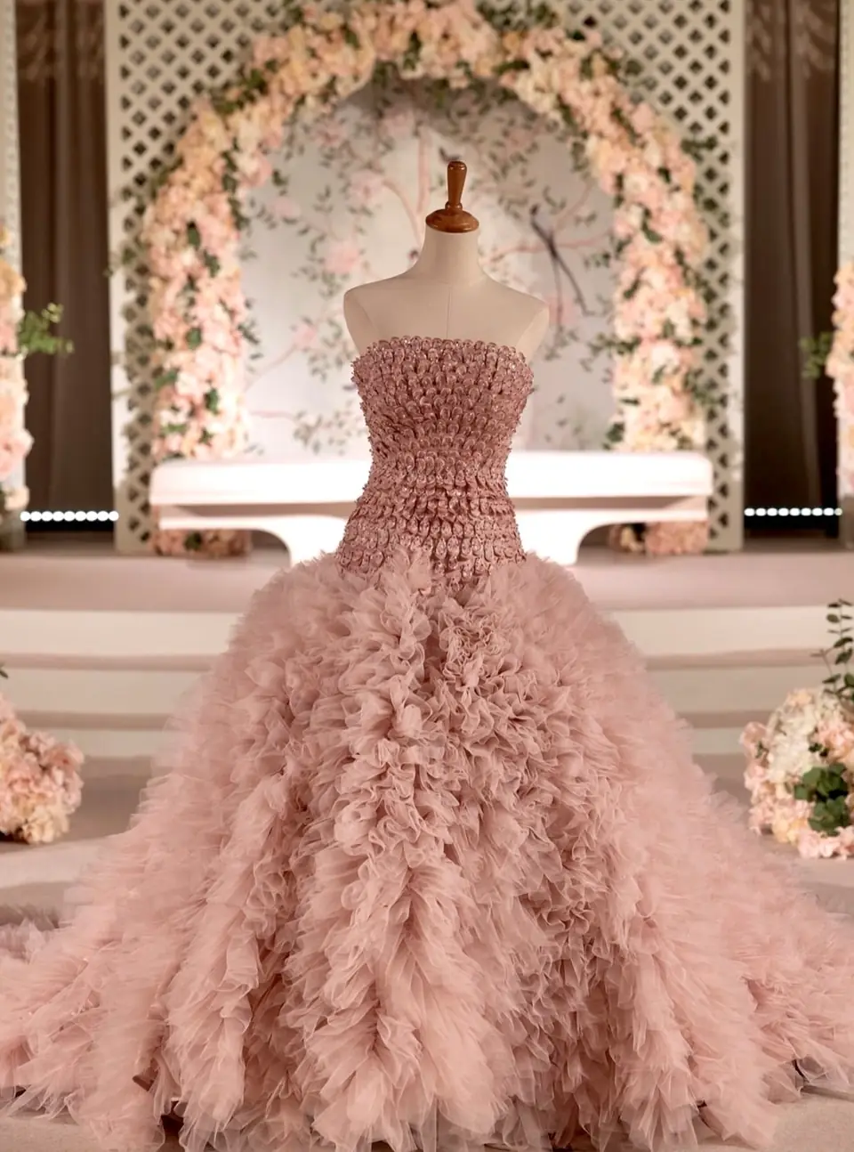 Strapless blush ball gown with petal-beaded bodice and ruffled tulle train on a dress form