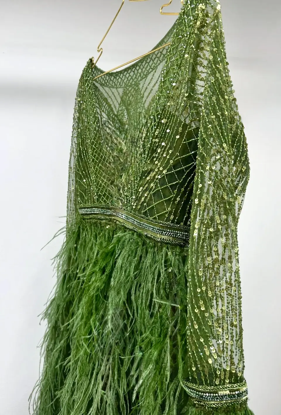 Detail of a green geometric beaded bodice, beaded waistband and ostrich feathers