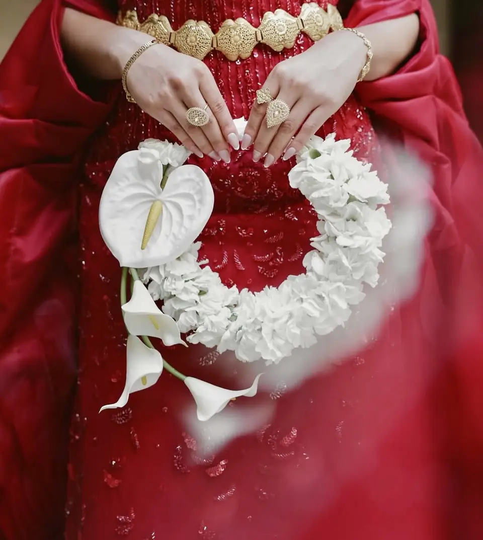 Red hand-beaded gown with a gold filigree belt and a white anthurium and carnation wreath bouquet