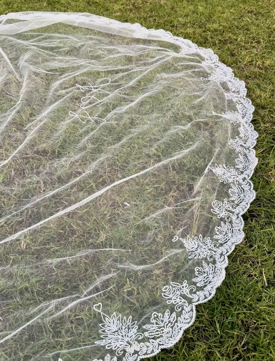 Scalloped lace-edged cathedral veil laid out on grass